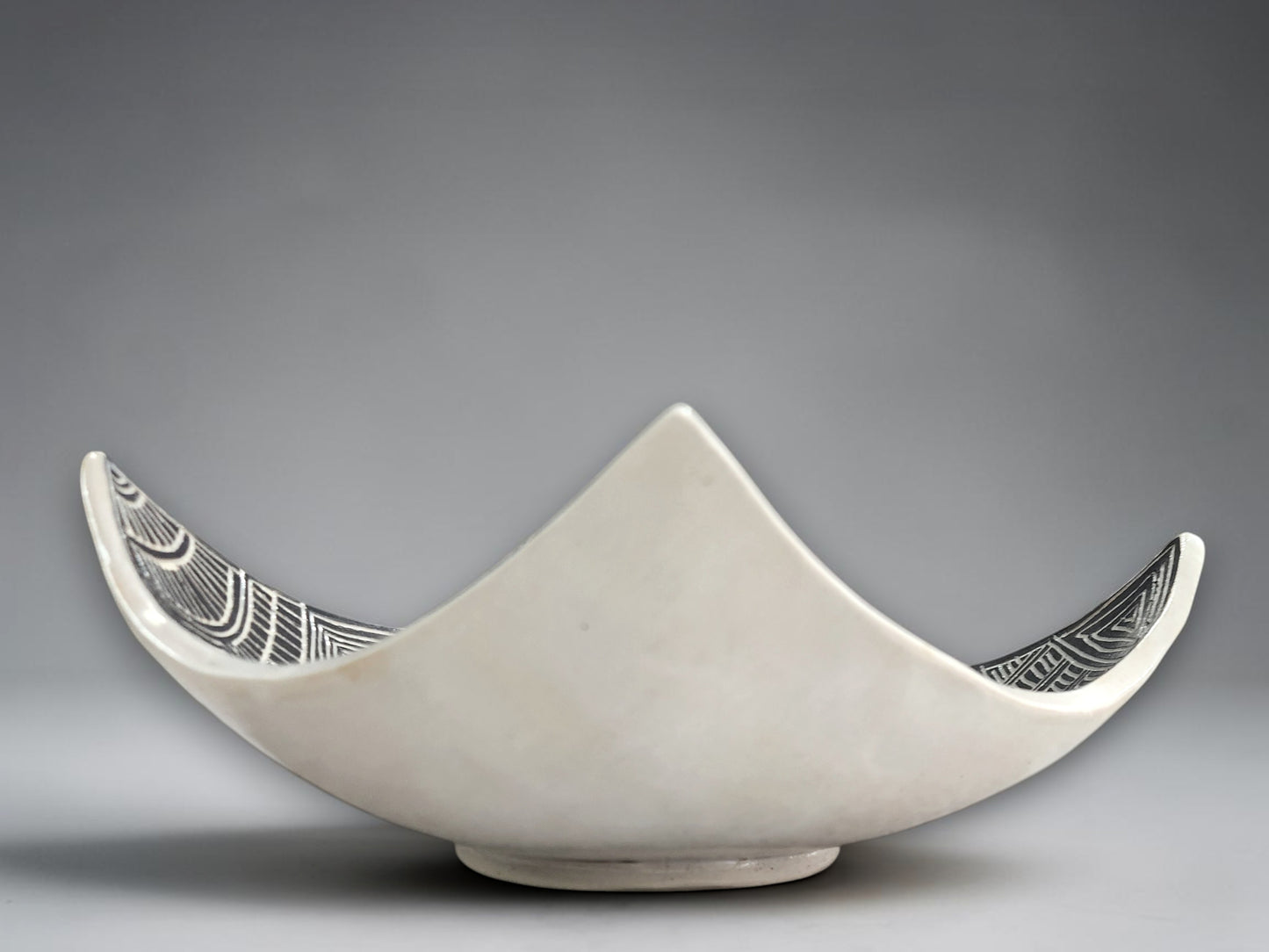 Handmade monochrome pottery bowl with elevated corners and engraved surface art