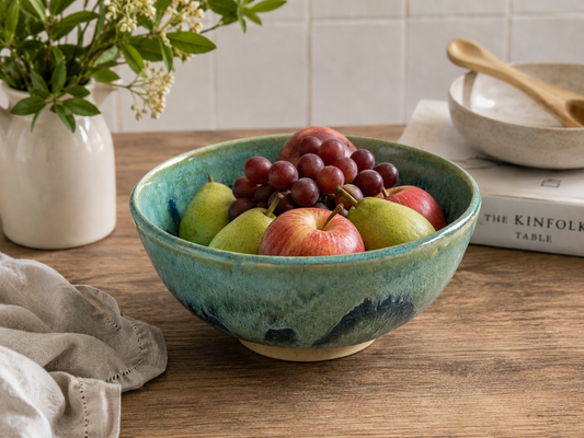 Handmade Australian ceramic fruit bowl in mottled green glaze displayed with fresh seasonal fruit in a contemporary kitchen setting by Buxton Pottery.