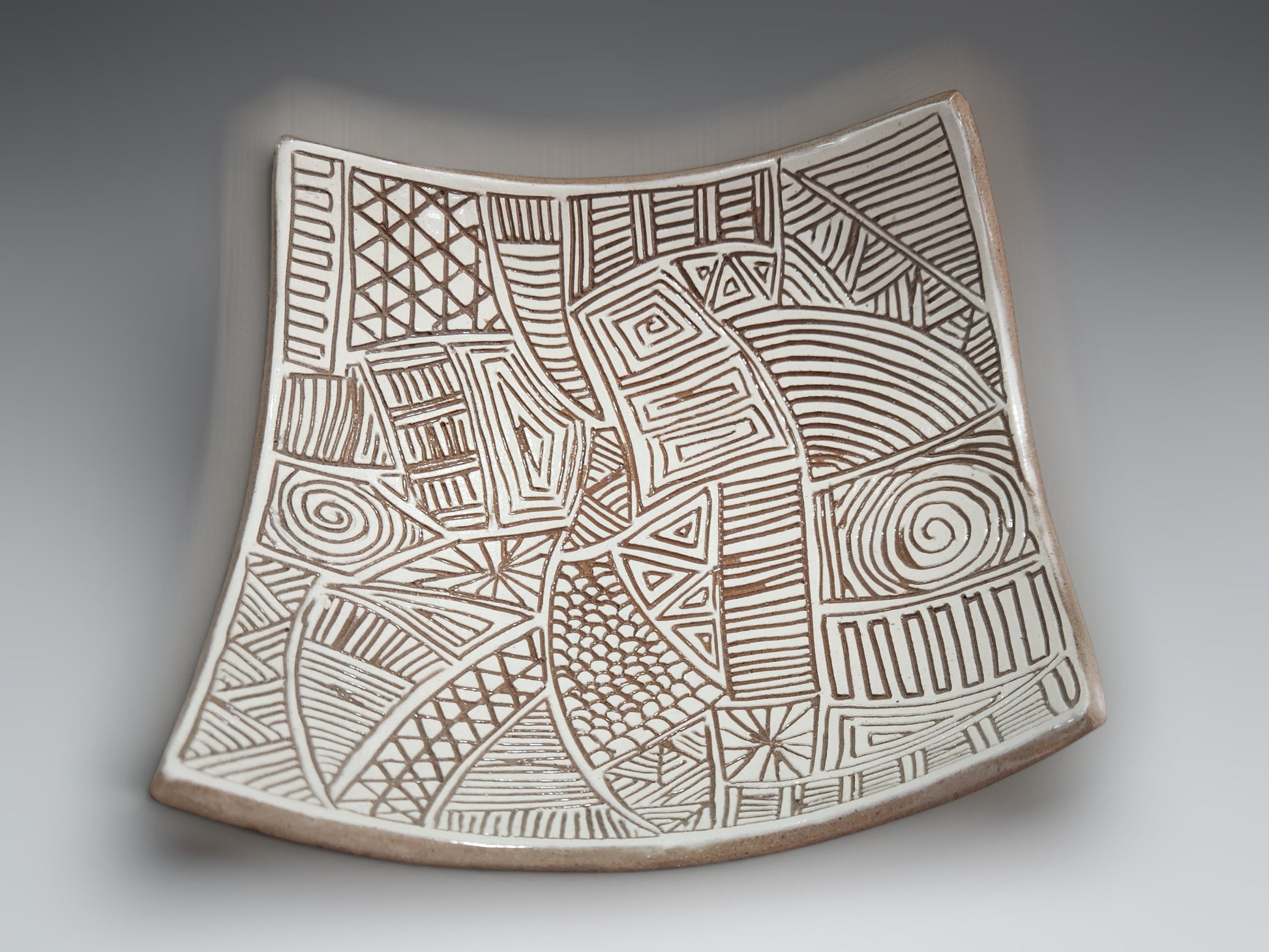 Handcrafted ceramic drape bowl carved into white slip with tribal-inspired geometric detailing