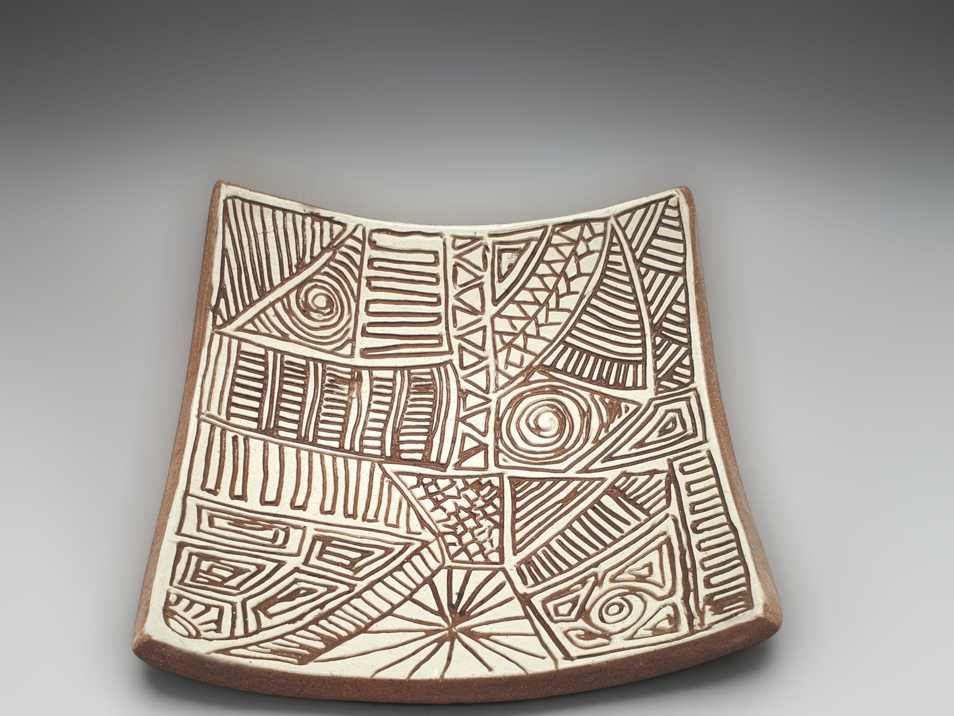 Small artisan pottery bowl with elevated corners and hand-etched geometric motifs