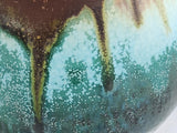 Close-up of the Bush Creek Earth glaze showing flowing turquoise, moss green and earthy brown on a handmade ceramic teacup
